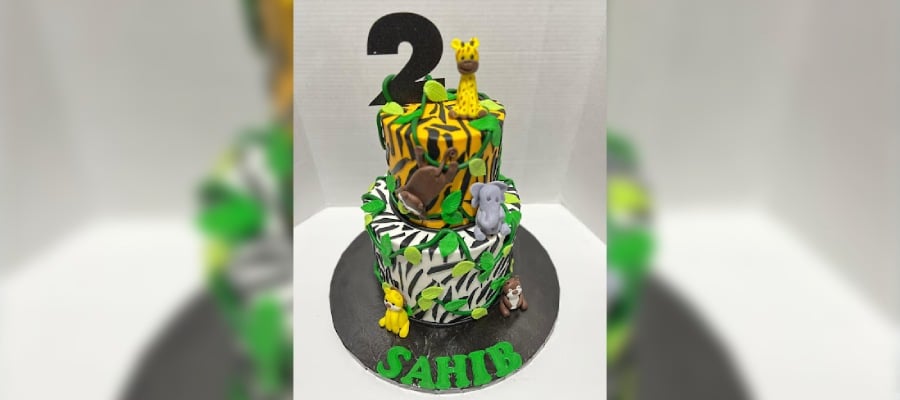 a colorful two-tiered jungle-themed custom birthday cake with animal prints and fondant figures, celebrating sahib's second birthday 