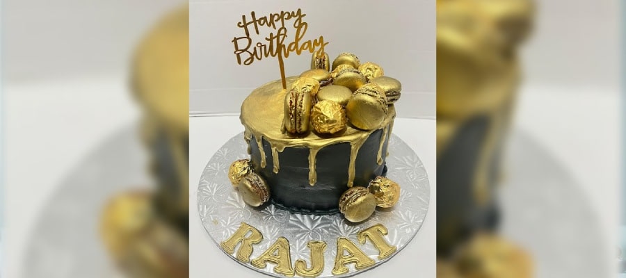 A luxurious black and gold-themed custom birthday cake adorned with golden macarons and topped with a 'happy birthday' topper