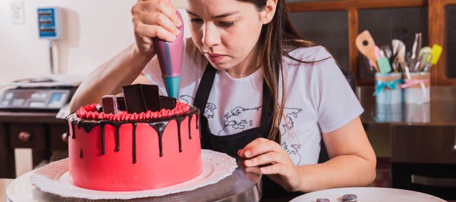 A young woman designing a cake, seems focused on her task, the cake is beautifully decorated with a drizzle of chocolate or glaze