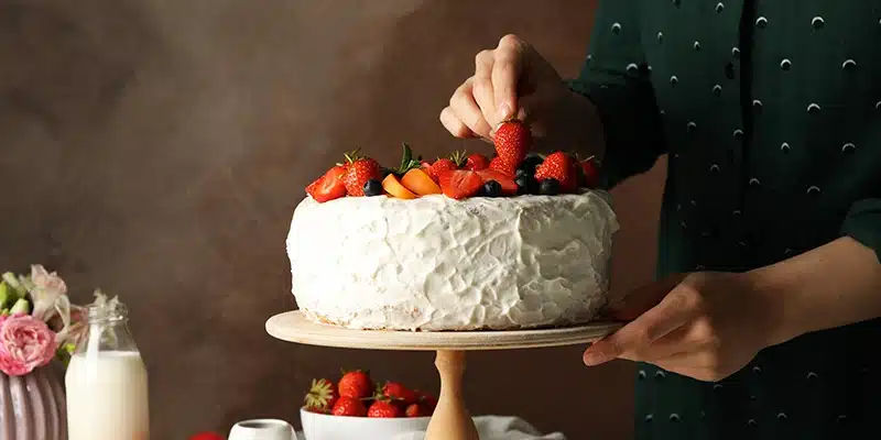 Person decorating a white frosted cake with fresh strawberries, highlighting the challenges in decorating store-bought and custom cakes.