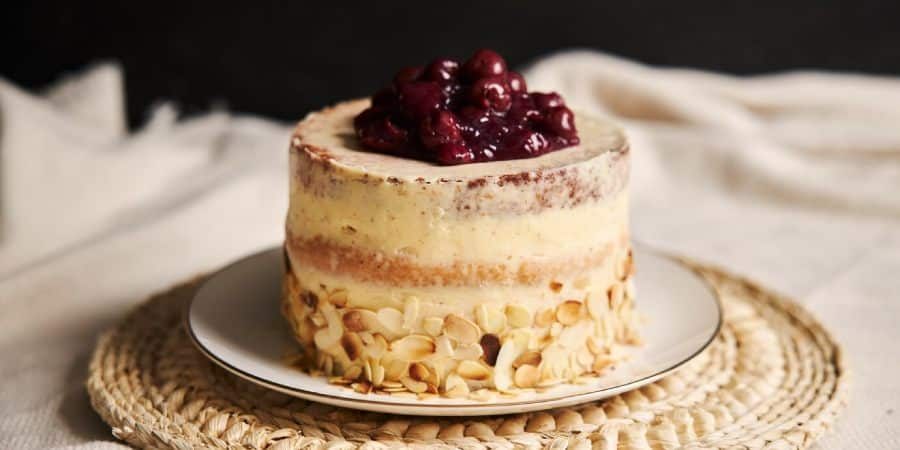 A rustic, low-calorie, naked-layer cake with creamy frosting, topped with a generous amount of cherries. The bottom edge is decorated with almond slices, offering a light indulgence.